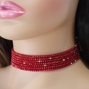 May include: A red beaded choker necklace with gold accents. The necklace is made of small, faceted beads and is layered for a bold look.