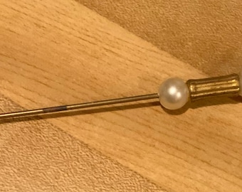 May include: A gold-toned stick pin with two white pearl accents. The pin has a sharp point on one end and a decorative, fluted design on the other end.