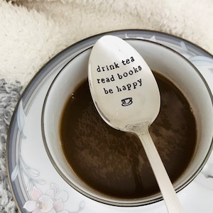 May include: A silver teaspoon with the inscription "drink tea read books be happy" and a small teacup icon.