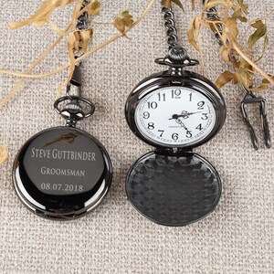 Puede incluir: Un reloj de bolsillo negro con una esfera plateada y agujas negras. El reloj est&aacute; grabado con el texto "STEVE GUTTBINDER GROOMSMAN 08.07.2018".