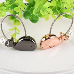 Puede incluir: Dos llaveros con forma de ballena con los nombres personalizados "Moses" y "Jamie" en los charms. Los charms de ballena están conectados a una cadena de cable plateada.
