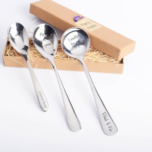 May include: Three stainless steel spoons with engraved text, presented in a brown gift box with straw. The spoons have text that reads "Papa's ice cream spoon", "I ureally love you so lets spoon", and "Laura Wolf" and "Rohab & Kev".