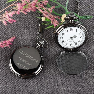 Puede incluir: Reloj de bolsillo negro con una esfera blanca y agujas negras. El reloj tiene una cadena. El reloj est&aacute; grabado con el texto "Steve Guttbinder, Groomsman, 08.07.2018".