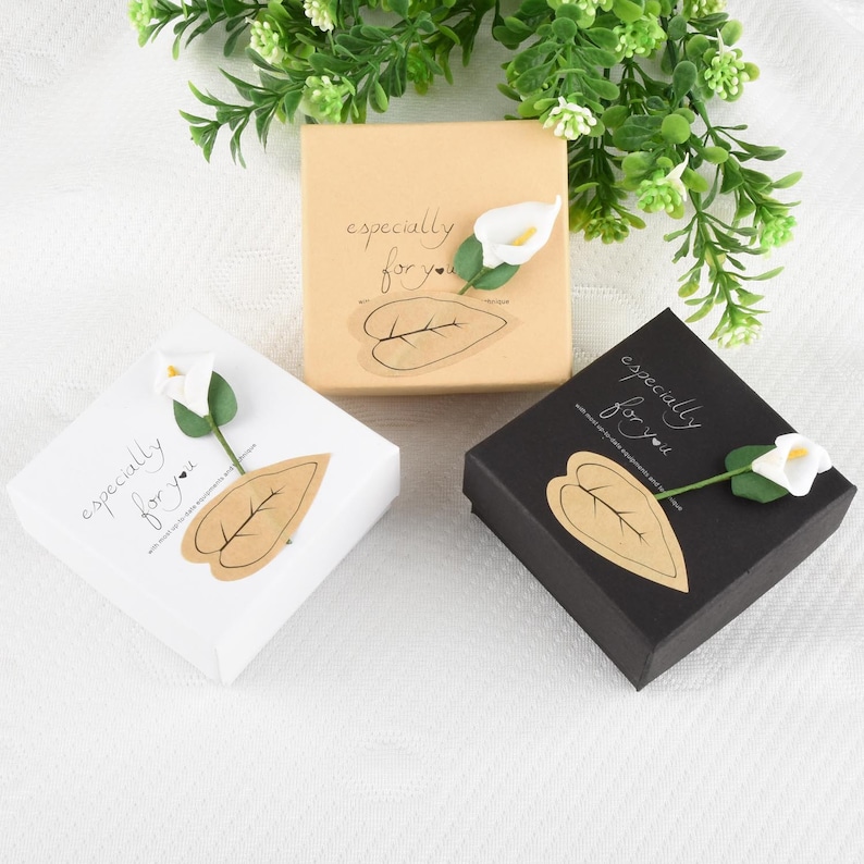 Op de afbeelding: Drie cadeaudozen met een witte calla lelie op elke doos. De dozen zijn wit, bruin en zwart. Elke doos heeft een bruine papieren bladsticker met de tekst "especially for you".