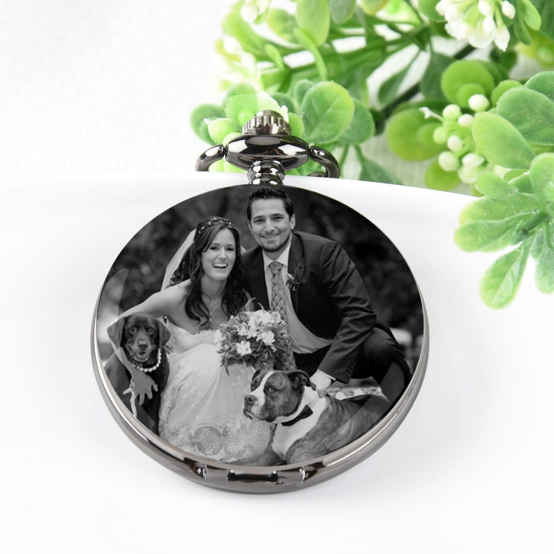 Puede incluir: Un reloj de bolsillo redondo de plata con una foto en blanco y negro de una pareja con dos perros.