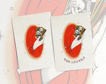 May include: Two rectangular art prints featuring a hand holding a deck of tarot cards. The central illustration shows a hand against a red oval background with star accents. The right print includes the text THE LOVERS in red lettering.