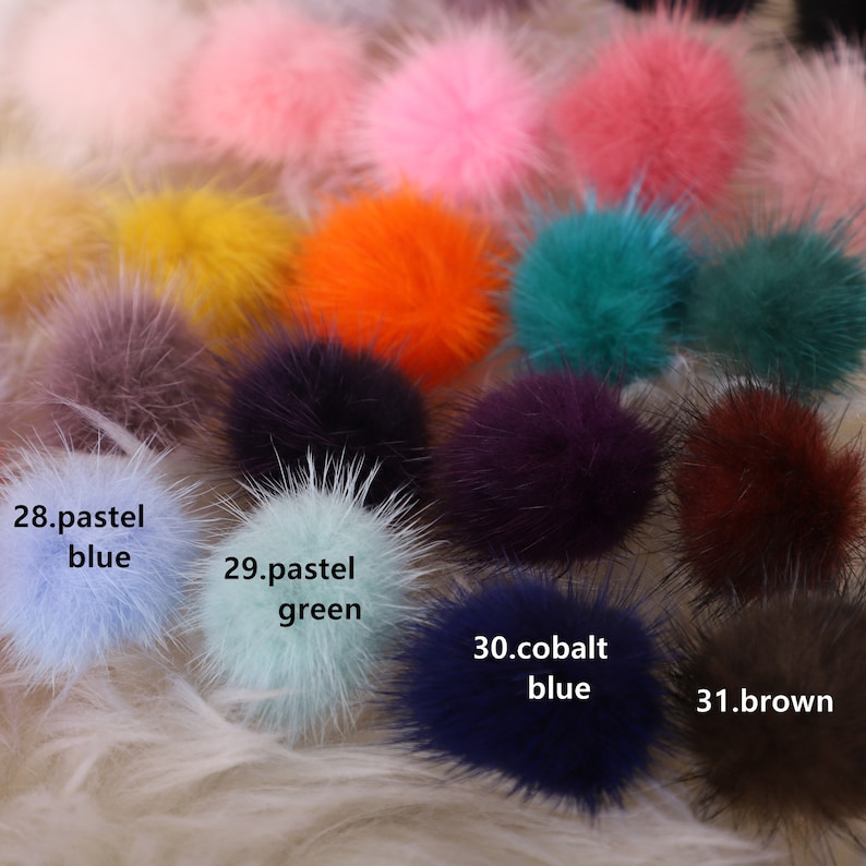 May include: A collection of colorful, fluffy pom-poms in various shades, including pink, orange, blue, and green. The image features pom-poms with the text "28. pastel blue", "29. pastel green", "30. cobalt blue", and "31. brown". The pom-poms are on a white, fluffy surface.