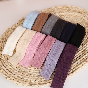 May include: A selection of colourful headbands in shades like light blue, brown, grey, black, and various pinks and purples. The headbands are displayed on a woven, circular basket, highlighting their textured, woven pattern.
