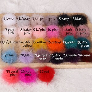 May include: A collection of 27 fluffy pom-poms in various colors, including ivory, gray, beige, navy, black, pink, yellow, orange, green, blue, purple, and red. Each pom-pom is labeled with a number and color name.