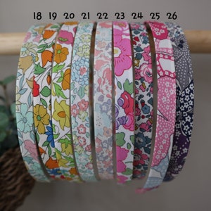 K&ouml;nnte beinhalten: Eine Auswahl an Haarreifen mit floralen Mustern in verschiedenen Farben, darunter Rosa, Blau, Gelb und Orange. Die Haarb&auml;nder werden auf einem Holzstab pr&auml;sentiert, der die verschiedenen Stoffdesigns hervorhebt. Die Nummern 18 bis 26 sind auf den Haarb&auml;ndern aufgedruckt.
