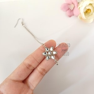 May include: A silver chain with a flower-shaped pendant featuring mirrored glass stones. The pendant is attached to a silver chain with a small ball at the end. The text "SPLENDID Jewel STUDIO" is visible in the image.