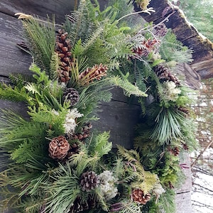 K&ouml;nnte beinhalten: Ein gr&uuml;ner, brauner und wei&szlig;er Weihnachtskranz aus Kiefern&auml;sten, Zapfen und anderen nat&uuml;rlichen Elementen.