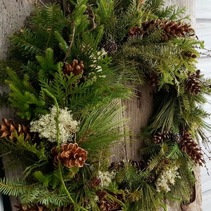 K&ouml;nnte beinhalten: Ein gr&uuml;ner Weihnachtskranz aus Kiefern-, Zedern- und anderen immergr&uuml;nen Zweigen. Der Kranz ist mit Tannenzapfen und anderen nat&uuml;rlichen Elementen verziert.