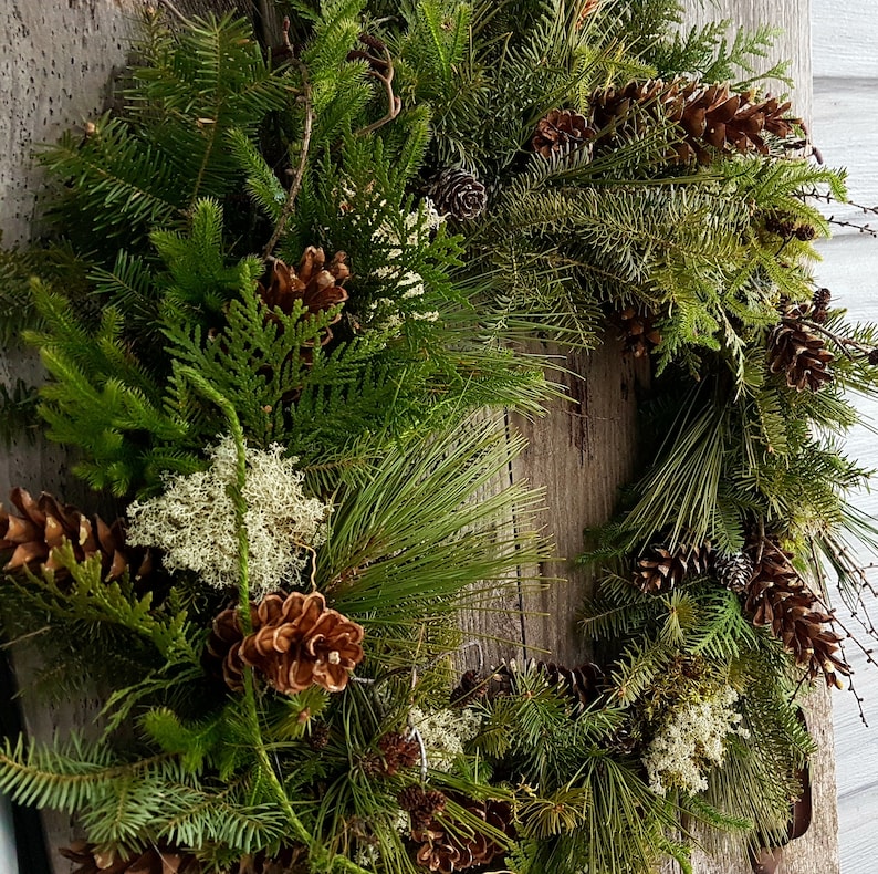 K&ouml;nnte beinhalten: Ein gr&uuml;ner Weihnachtskranz aus Kiefern-, Zedern- und anderen immergr&uuml;nen Zweigen. Der Kranz ist mit Tannenzapfen und anderen nat&uuml;rlichen Elementen verziert.