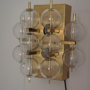 May include: A vintage wall sconce featuring clear glass globes and brass accents. The fixture has a rectangular brass base with multiple glass spheres attached with brass rods. The design is a mid-century modern style.