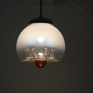 May include: A vintage pendant light fitting with a frosted glass globe. The light has a clear glass lower section with decorative elements and a dark metal cap. The fitting hangs from a black rod and a wire.
