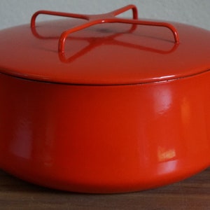May include: A bright orange enamel pot with a lid and two handles. The pot has a metal wire rack on top of the lid.