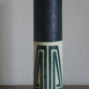 May include: A tall, cylindrical ceramic vase with a dark blue glaze and white and green geometric designs. The vase has a wide base and a narrow neck.