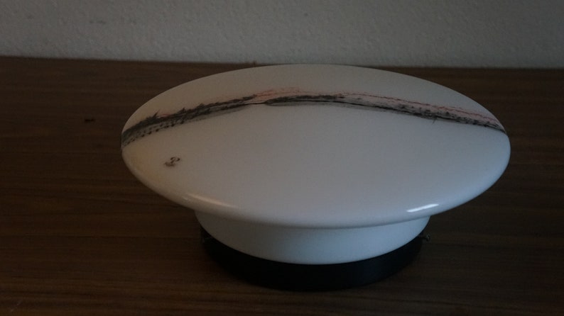 K&ouml;nnte beinhalten: Wei&szlig;er Keramik-Lampenschirm mit einem abstrakten Design in Schwarz und Rosa. Der Lampenschirm ist an einem schwarzen Sockel befestigt.
