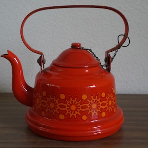 Op de afbeelding: Een rode emaille theepot met een geometrisch patroon in oranje. De theepot heeft een scharnierend deksel en een metalen handvat.