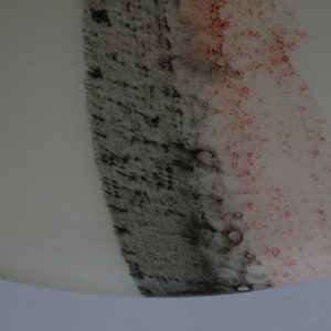 K&ouml;nnte beinhalten: Nahaufnahme einer wei&szlig;en Keramikplatte mit einem schwarzen und rosafarbenen Streifen, der darauf gemalt ist. Der Streifen besteht aus kleinen Punkten und hat eine strukturierte Optik.