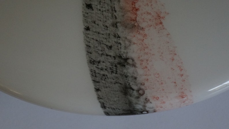 K&ouml;nnte beinhalten: Nahaufnahme einer wei&szlig;en Keramikplatte mit einem schwarzen und rosafarbenen Streifen, der darauf gemalt ist. Der Streifen besteht aus kleinen Punkten und hat eine strukturierte Optik.