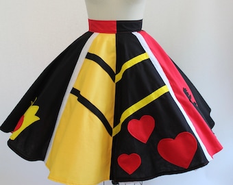 May include: A full-circle skirt featuring a color-blocked design in black, yellow, red, and white panels. The skirt includes black chevron-style stripes and red heart-shaped appliqués on the black sections, with a solid red and black waistband.
