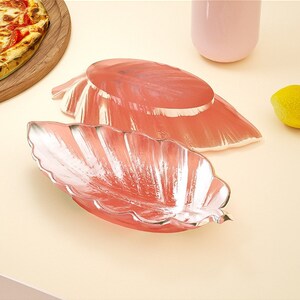 May include: Two pink leaf-shaped serving dishes with a metallic silver finish. The dishes are made of ceramic and have a glossy finish.