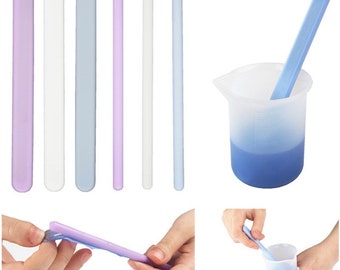 May include: Set of six silicone spatulas in various colors, including purple, white, and blue. The spatulas are flexible and have a rounded tip. They are shown in a variety of positions, including being held in hands and used to stir a blue liquid in a clear measuring cup.