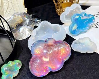 May include: A set of four silicone molds shaped like clouds. The molds are translucent and have a shiny, iridescent finish.