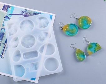 May include: A clear silicone mold with various shapes for resin art, alongside finished resin earrings. The earrings feature a teal, gold, and green marbled design. The mold includes circles, ovals, and other geometric shapes for crafting jewelry.