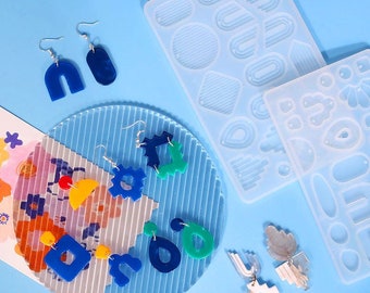 May include: Two silicone molds for making earrings. The molds are clear and feature various geometric shapes, including circles, squares, and arches. The molds are shown with finished earrings made from resin in various colors, including blue, green, and yellow.