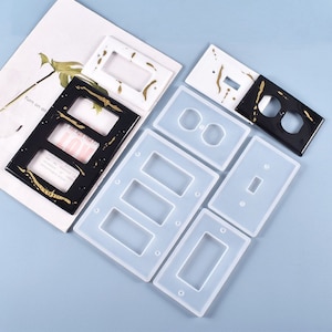 May include: A set of six silicone moulds for making decorative light switch and outlet covers. The moulds are white and feature different shapes for single, double, and triple switch covers.