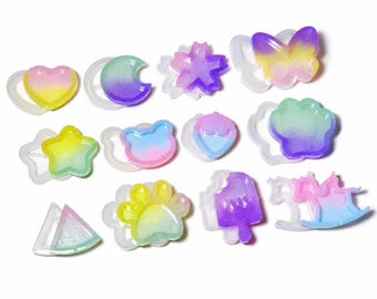 May include: A collection of silicone molds for resin crafting, each paired with a finished colorful gradient resin piece. Shapes include a heart, crescent moon, cherry blossom, butterfly, star, bear head, strawberry, paw print, watermelon slice, popsicle, and rocking horse.