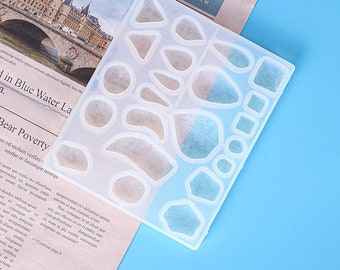 May include: A clear silicone mold with 18 different shapes for crafting. The shapes include circles, ovals, squares, and irregular shapes.