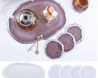 May include: Set of four round silicone molds for making agate coasters. The molds are white and have a smooth, rounded edge. The molds are shown next to a finished set of agate coasters in shades of pink and white.