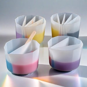 May include: Four clear plastic cups with dividers, each filled with different coloured liquids. The cups are designed for making layered desserts or drinks.