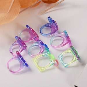 May include: Assortment of colourful plastic rings with different shapes. The rings are translucent and have a sparkly finish.