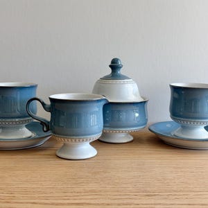 May include: A tea set consisting of two cups with matching saucers, a creamer, and a lidded sugar bowl. Each piece features a gradient blue finish, a white pedestal base, and a delicate white beaded pattern along the rim and base edges.