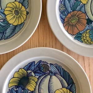 May include: Three white ceramic plates with a blue, yellow, and green floral design. The plates feature a stylized pumpkin and flowers.