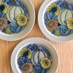 May include: Three white ceramic plates with a blue, yellow, and green floral design featuring a stylized pumpkin in the center.