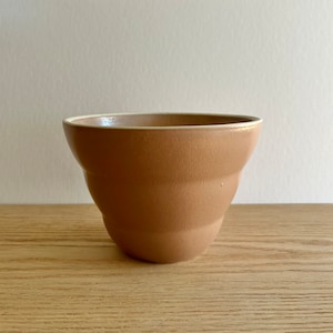 Könnte beinhalten: Eine braune Keramikschüssel mit weißem Rand. Die Schüssel hat ein geriffeltes Design und steht auf einer Holzoberfläche.