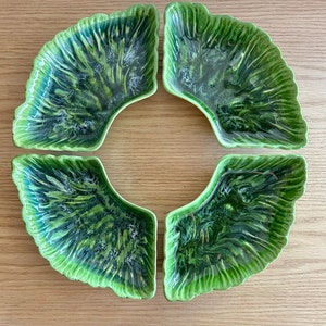 Puede incluir: Juego de cuatro platos para servir de cerámica verde y blanca con forma de hojas. Los platos están dispuestos en círculo, con las puntas de las hojas hacia adentro.