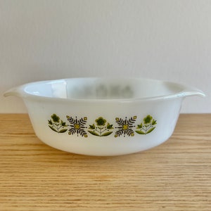 Puede incluir: Plato para hornear de cerámica blanca con un patrón floral verde y amarillo. El plato tiene dos asas.