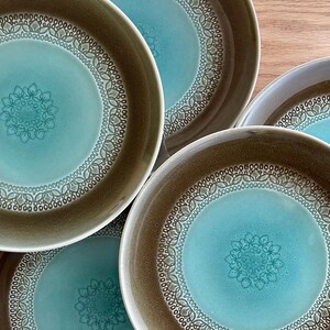 May include: A collection of five ceramic bowls. Each bowl has a teal centre with a floral pattern and a decorative border. The rims are brown. The bowls are arranged on a wooden surface.