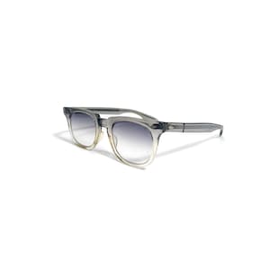 May include: Gray sunglasses with a gradient lens. The frames are a translucent gray, and the lenses transition from a dark gray at the top to a lighter tint at the bottom. The sunglasses have a classic, square shape.