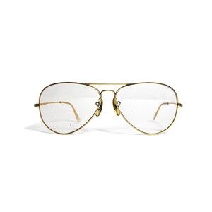Puede incluir: Gafas de sol de aviador con montura dorada y lentes transparentes. Las gafas tienen un doble puente y varillas finas. Las lentes tienen forma de l&aacute;grima y la montura es de color dorado brillante. Sobre fondo blanco.