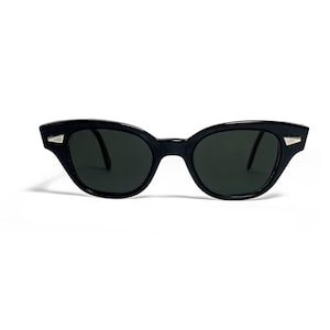 May include: Black cat-eye sunglasses with dark lenses. The frames are a glossy black with small silver accents on the outer corners. The sunglasses have a classic, retro design.