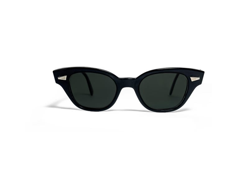 May include: Black cat-eye sunglasses with dark lenses. The frames are a glossy black with small silver accents on the outer corners. The sunglasses have a classic, retro design.