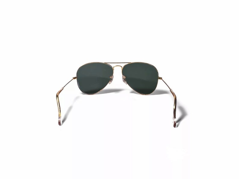May include: Gold aviator sunglasses with dark green lenses. The sunglasses are folded in half with the arms pointing upwards.